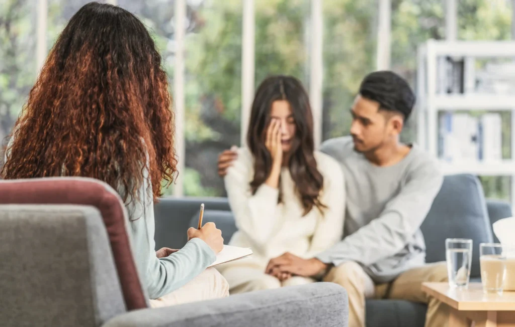 Couple sitting together on a couch, talking with concern and care.